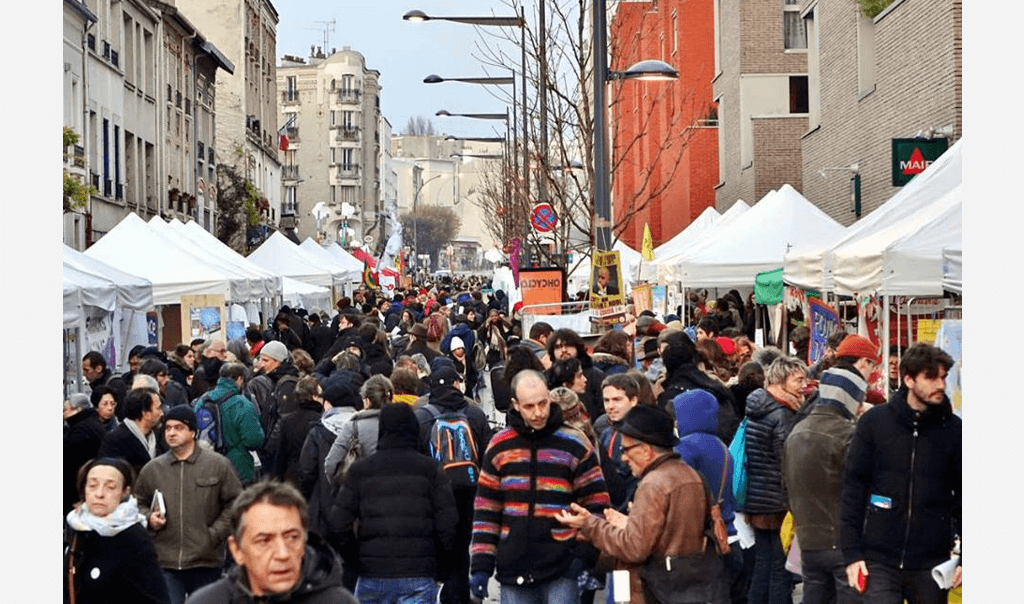 Foule entre des stands dans le Village Mondial des Alternatives