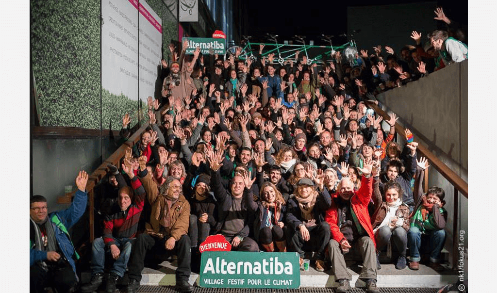 Foule assis sur un escalier avec affiche "Bienvenue, Alternatiba village festif pour le climat"
