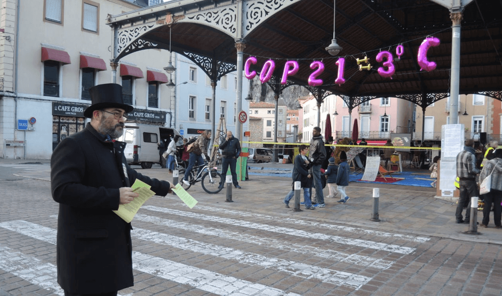 Un homme qui tend des prospectus devant un stand "COP21 - 3°C"