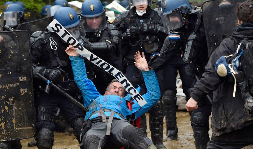 Un homme portant une banderole "Stop violence" qui est mis à terre par un groupe de policiers